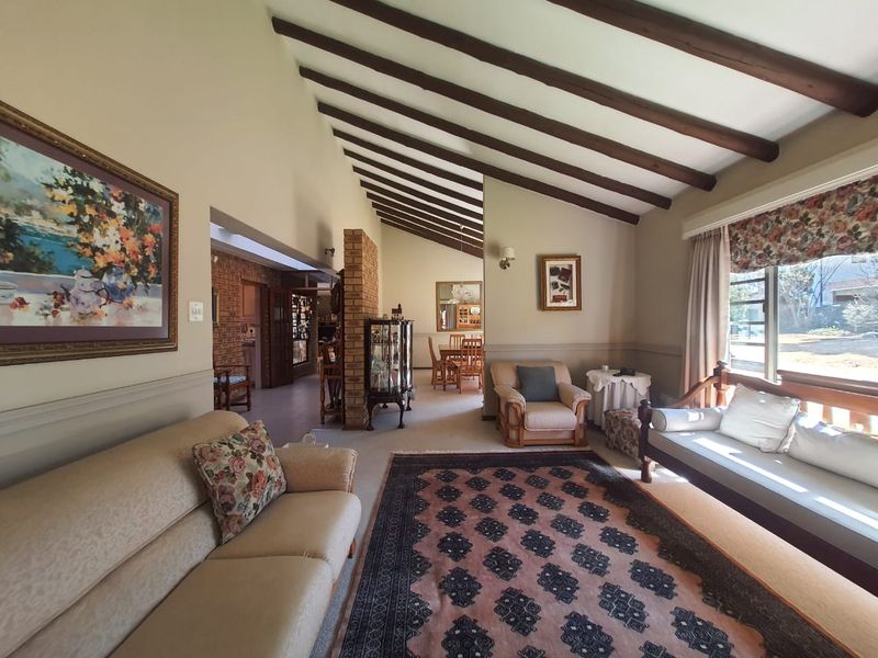 Spacious living room featuring a vaulted ceiling with exposed timber beams, a brick feature wall, and large windows providing natural light.