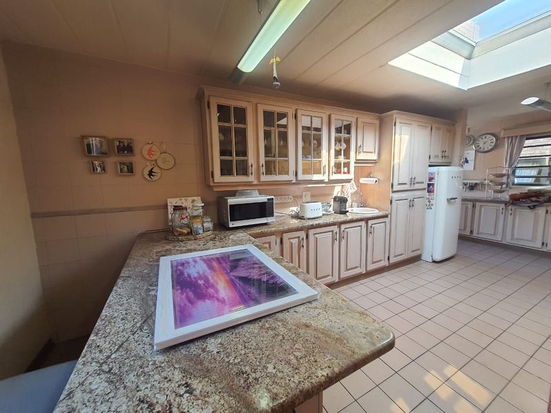 Spacious kitchen featuring granite countertops, ample built-in cabinetry, tiled flooring, and a skylight that provides natural light.