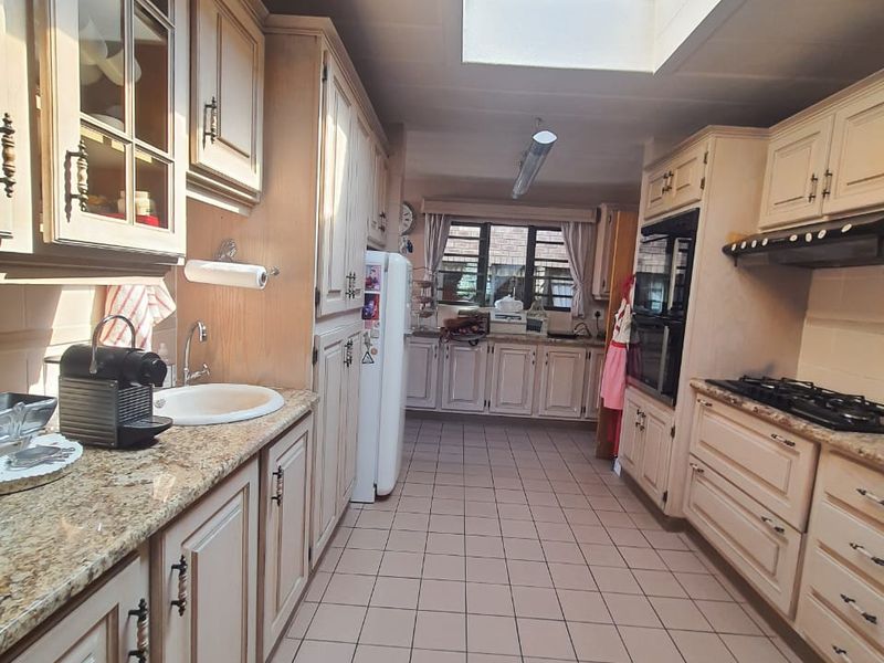 Spacious kitchen featuring light wood cabinetry, granite countertops, integrated appliances, and a large skylight providing ample natural light.