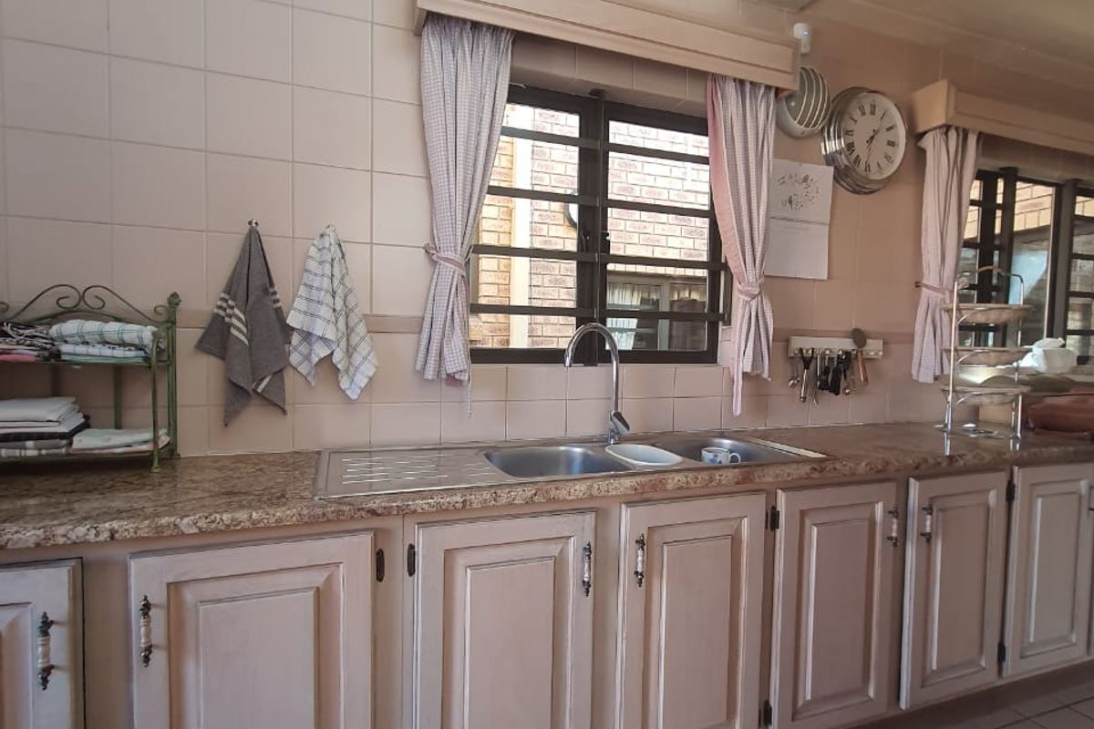 A functional kitchen featuring granite countertops, a double basin sink, tiled backsplash, and traditional built-in cabinetry with tiled flooring.