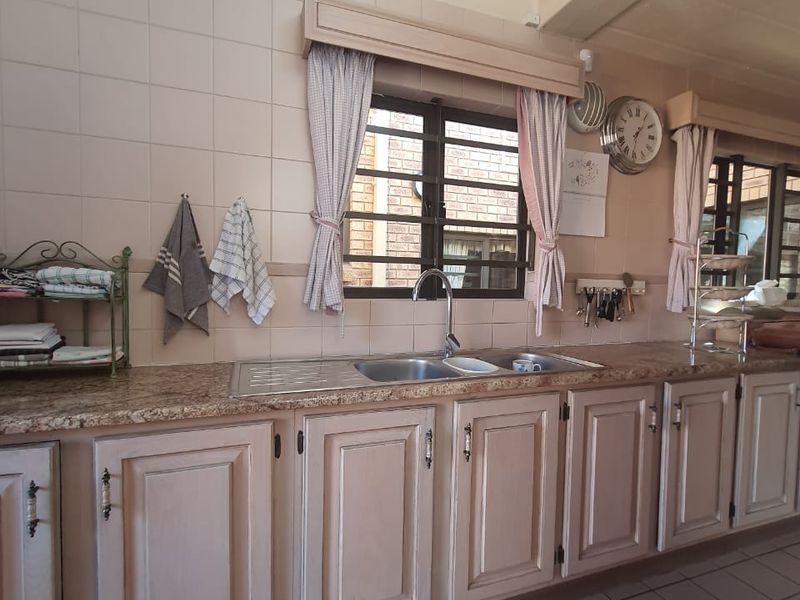 A functional kitchen featuring granite countertops, a double basin sink, tiled backsplash, and traditional built-in cabinetry with tiled flooring.