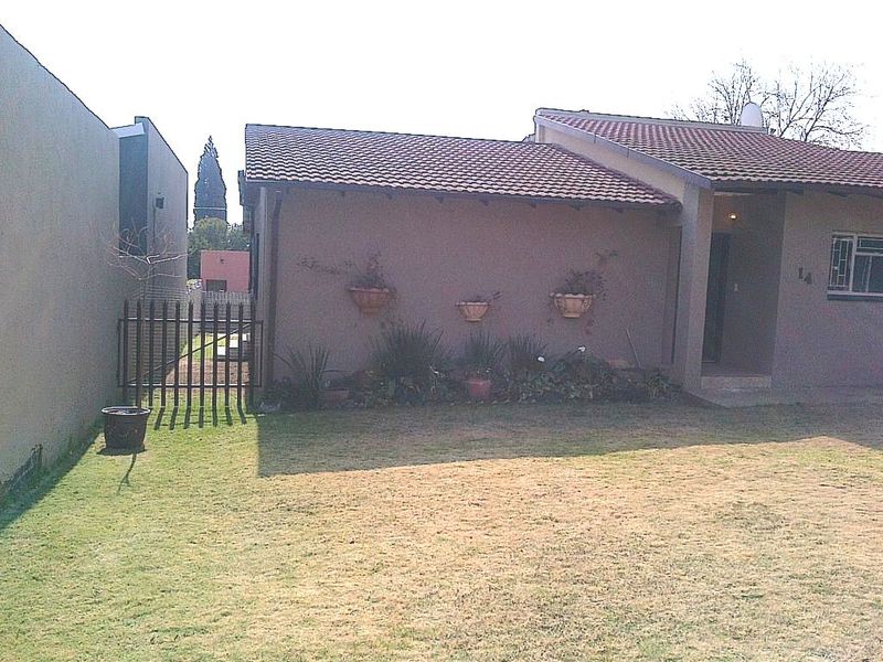 Front view of a residential house featuring a tiled roof, plastered exterior walls, and a metal security gate leading to the side yard.