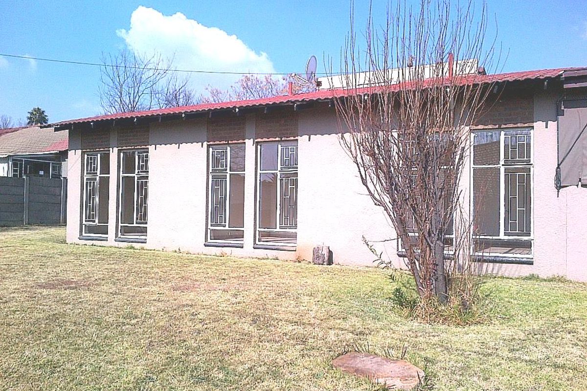 Rear view of the property featuring a metal roof, large windows with security bars, and a spacious backyard area.