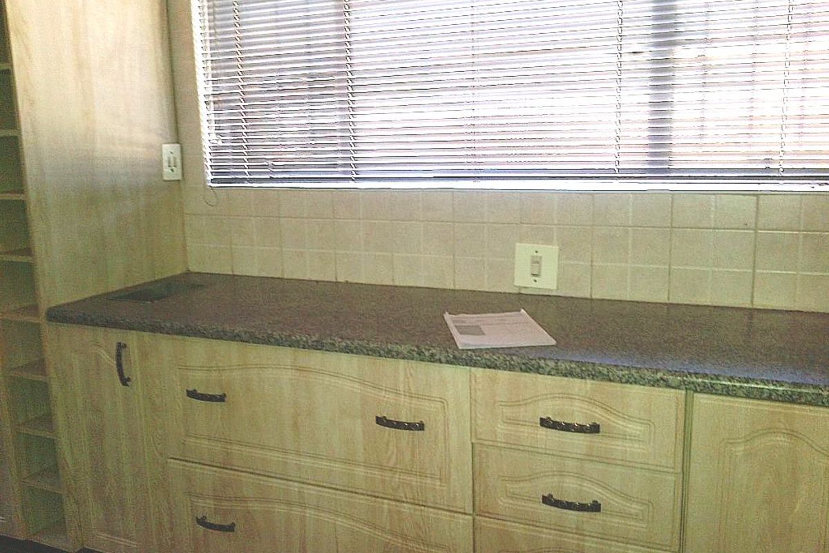 A functional kitchen area featuring light wood-grain cabinetry, a durable countertop, tiled backsplash, and venetian blinds for light control.
