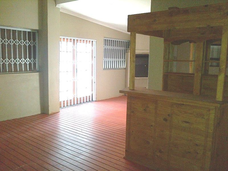 Covered patio area featuring wooden decking, security gates, and a built-in wooden bar, providing a functional outdoor entertainment space.