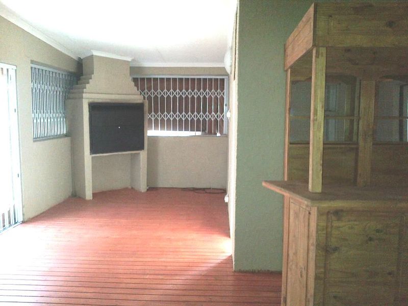 Covered patio area featuring timber decking and a built-in braai, secured with metal security gates.