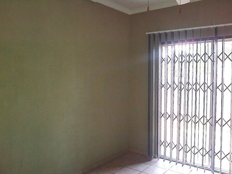An empty living room featuring tiled flooring, a ceiling fan, and a sliding door with a security gate leading to the exterior.