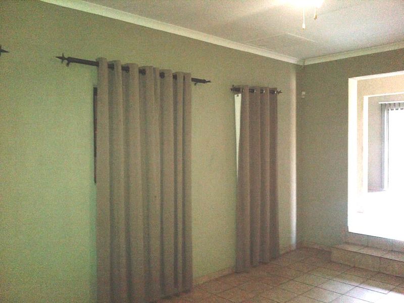 An empty living room featuring tiled flooring, neutral wall paint, and installed curtain rods, offering a blank canvas for interior design.