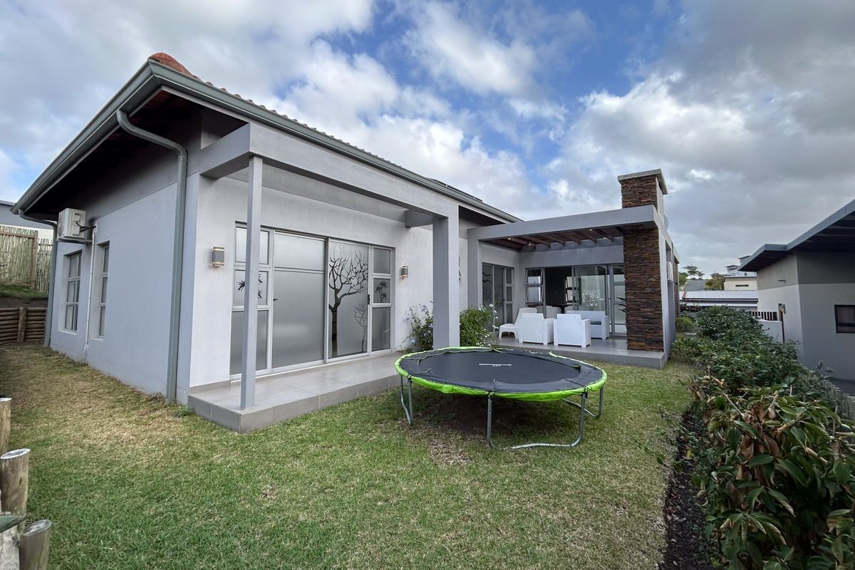 Rear view of the house featuring a covered patio with a stone-clad chimney, sliding glass doors, and a landscaped garden area.