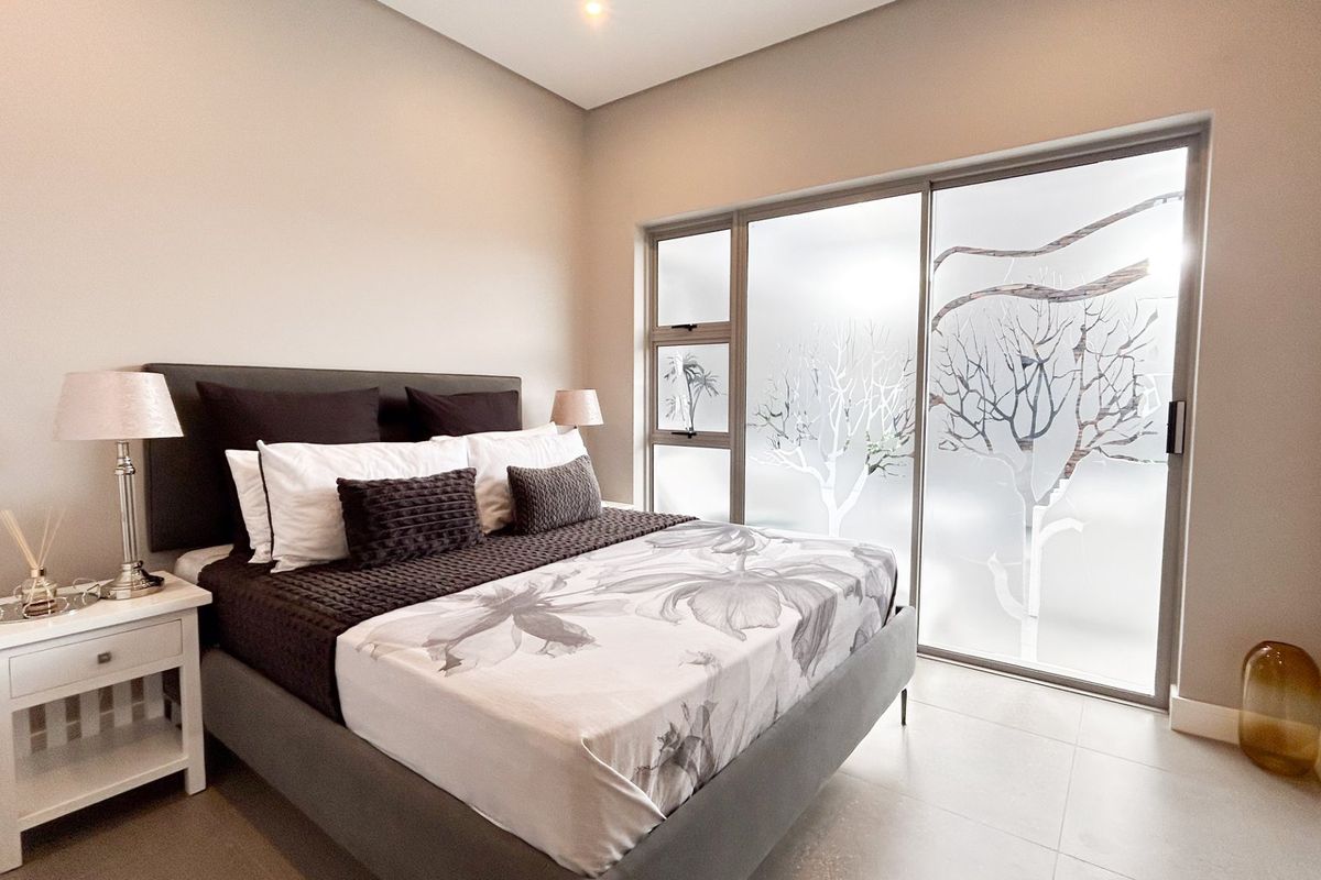 A well-maintained bedroom featuring neutral wall tones, large format floor tiles, and a sliding glass door with decorative frosted privacy film.