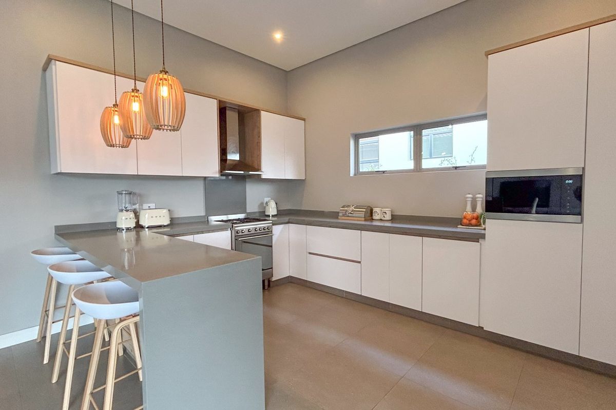Modern kitchen featuring sleek white cabinetry, stone countertops, a breakfast bar, integrated oven, and a built-in microwave, finished with contemporary pendant lighting.