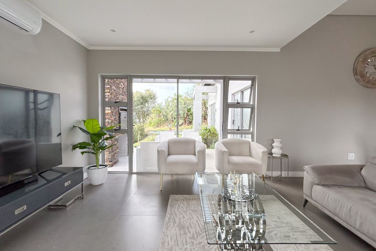 A bright and modern living room featuring large sliding glass doors that open onto a patio, with neutral tiled flooring and a wall-mounted air conditioner.