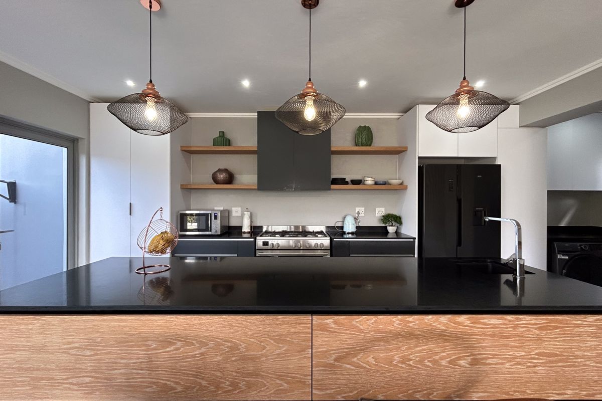 Modern kitchen featuring a large central island with timber cabinetry, black stone countertops, built-in stainless steel oven, and open shelving.