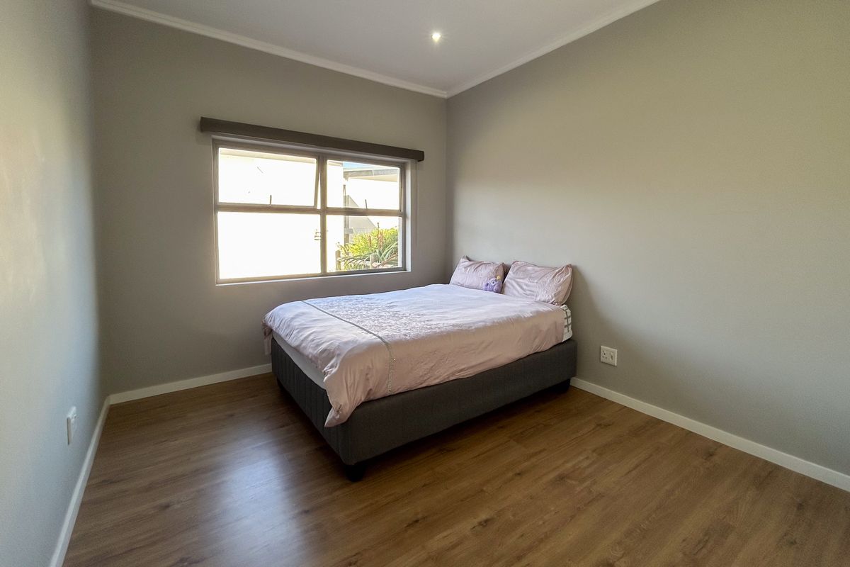 A well-maintained bedroom featuring modern laminate flooring, neutral wall tones, and a large window providing natural light.