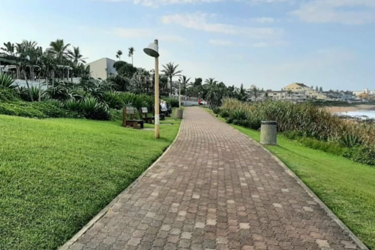 A scenic paved coastal walkway adjacent to a well-maintained lawn, offering direct access to the beach and surrounding coastal landscape.