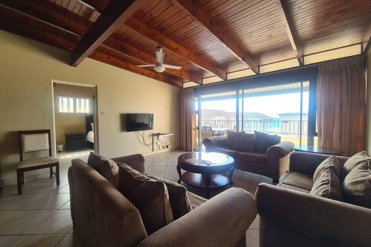 Spacious living area featuring exposed timber beam ceilings, tiled flooring, and large sliding glass doors opening onto a balcony with ocean views.