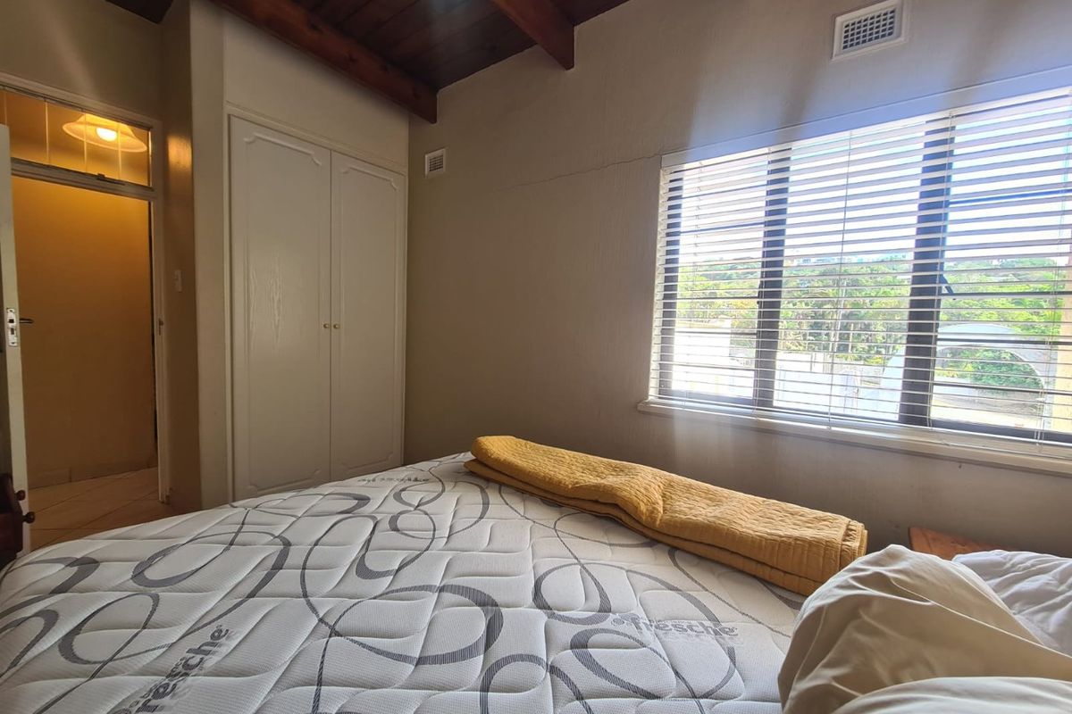A bedroom featuring exposed timber ceiling beams, built-in cupboards, and a window with horizontal blinds.