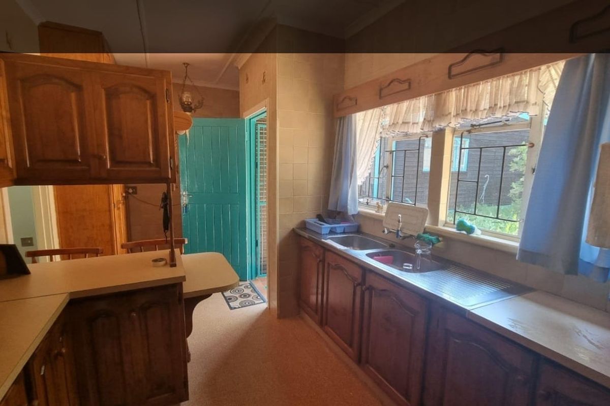 A dated kitchen featuring traditional wooden cabinetry, a double stainless steel sink, and a breakfast bar area with direct access to an exterior door.