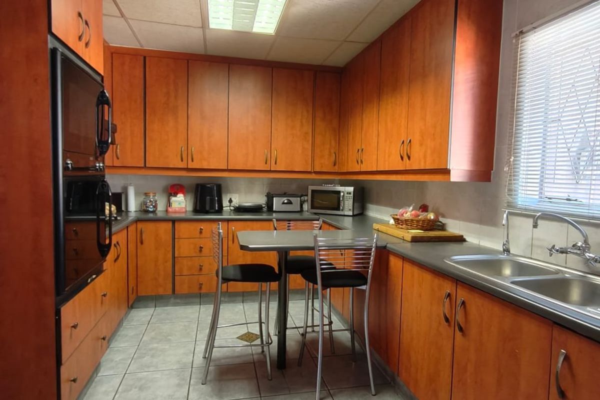 A functional kitchen featuring wood-tone cabinetry, integrated oven, double sink, and tiled flooring with a central breakfast nook area.