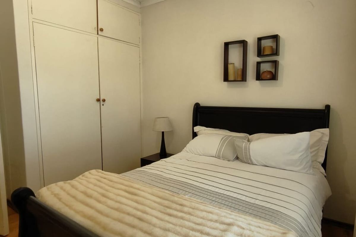 A cozy bedroom featuring built-in floor-to-ceiling cupboards and warm-toned timber flooring.