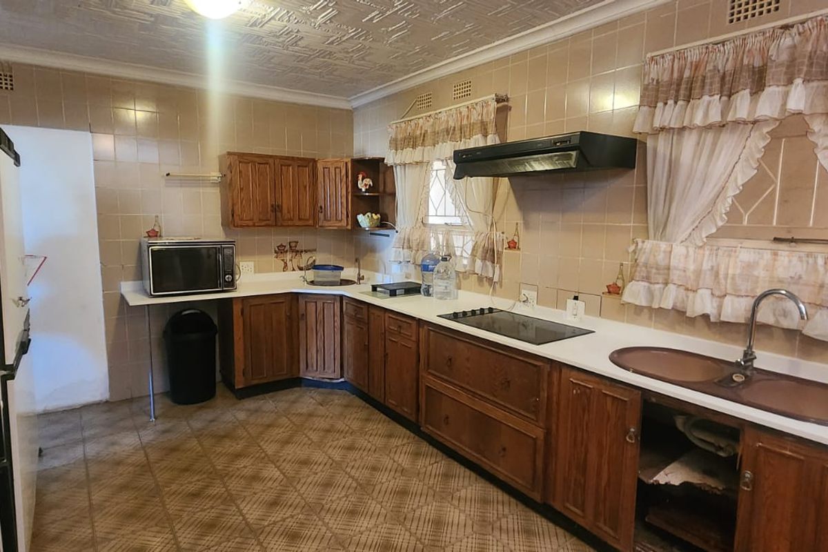 A dated kitchen featuring wood-finish cabinetry, tiled walls, a built-in hob, extractor fan, and a double sink with a gooseneck faucet.
