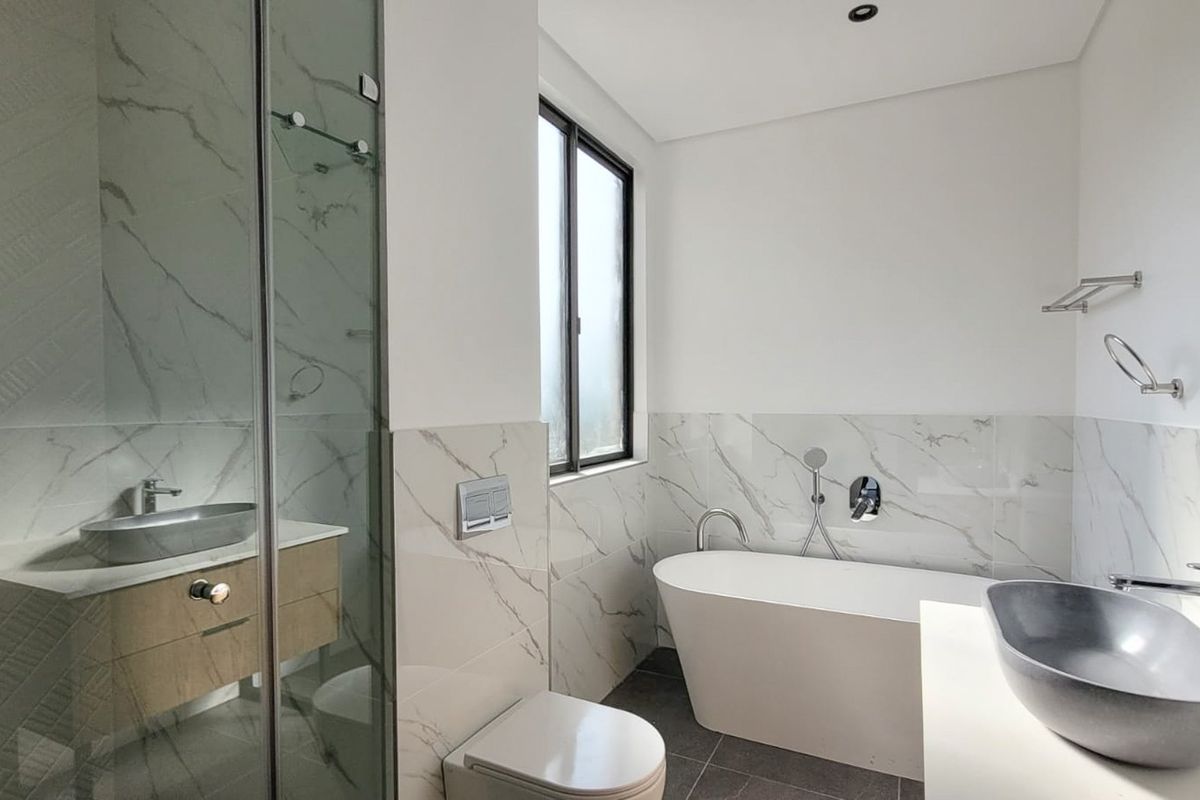 Modern bathroom featuring a freestanding bathtub, glass-enclosed shower, wall-mounted toilet, and dual vessel sinks with marble-look wall tiling.