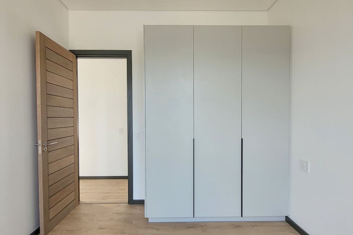 A clean, modern bedroom featuring built-in floor-to-ceiling cabinetry with a minimalist design and wood-look flooring.