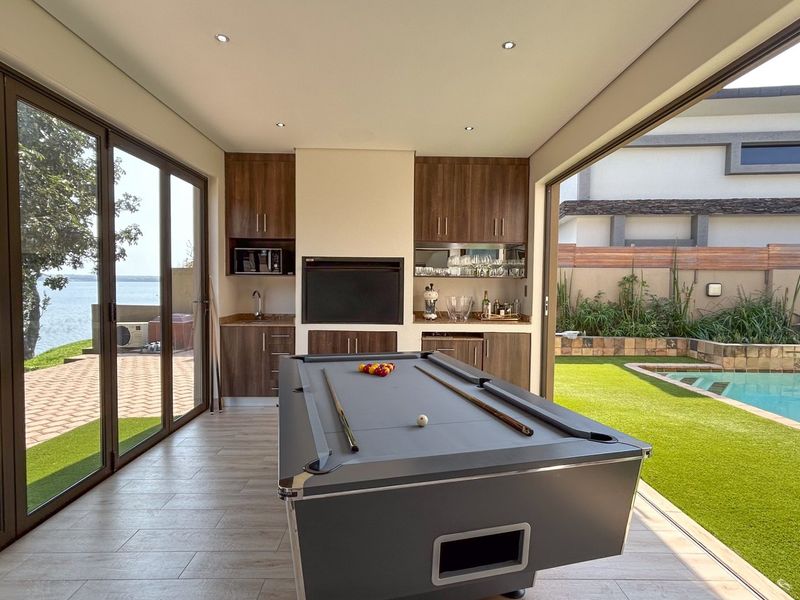 Modern entertainment bar area featuring built-in cabinetry, a sink, and a built-in braai, with seamless indoor-outdoor flow to the pool area.