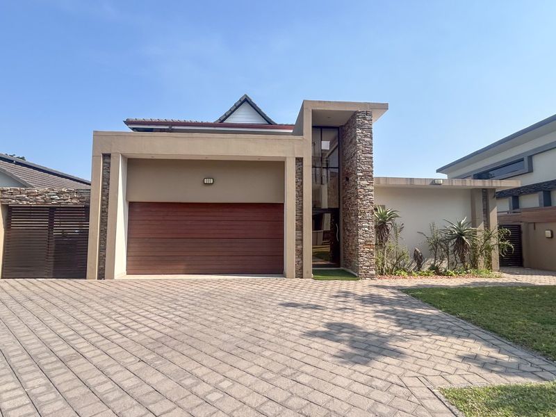 Modern front facade featuring a double garage with timber door, stone cladding accents, and a neatly paved driveway.