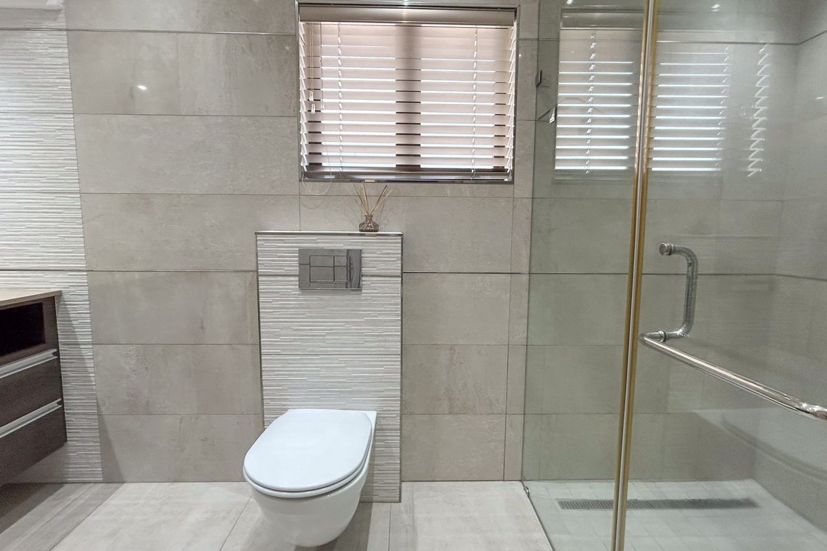 Modern bathroom featuring a wall-mounted toilet, glass shower enclosure, and contemporary tiled finishes with a vanity cabinet.
