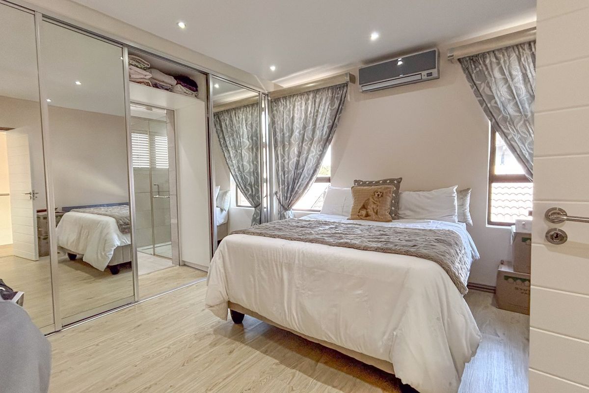 A well-maintained bedroom featuring mirrored sliding wardrobes, laminate flooring, recessed lighting, and a wall-mounted air conditioning unit.