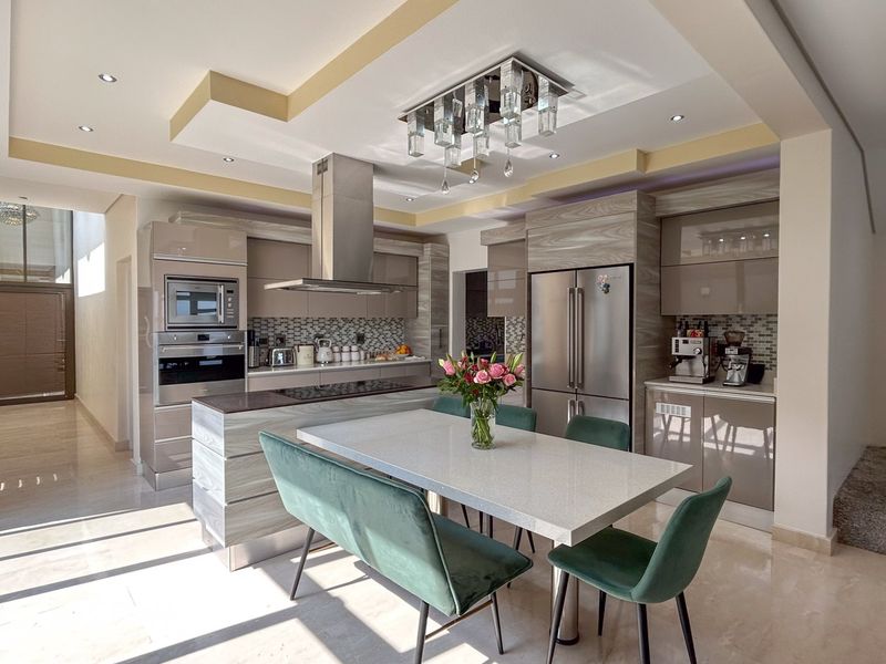 Modern open-plan kitchen featuring high-gloss cabinetry, stone countertops, a central island, built-in appliances, and a sophisticated coffered ceiling with recessed lighting.