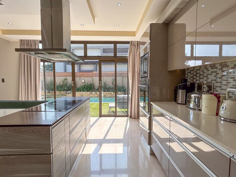 Modern open-plan kitchen featuring high-gloss cabinetry, stone countertops, integrated appliances, and seamless flow to the outdoor pool area through large sliding glass doors.