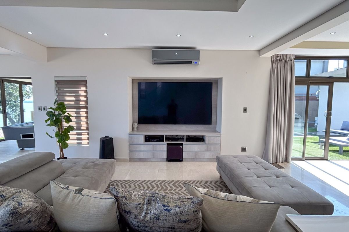 Spacious living room featuring built-in media cabinetry, recessed lighting, wall-mounted air conditioning, and large sliding glass doors providing access to the outdoor area.