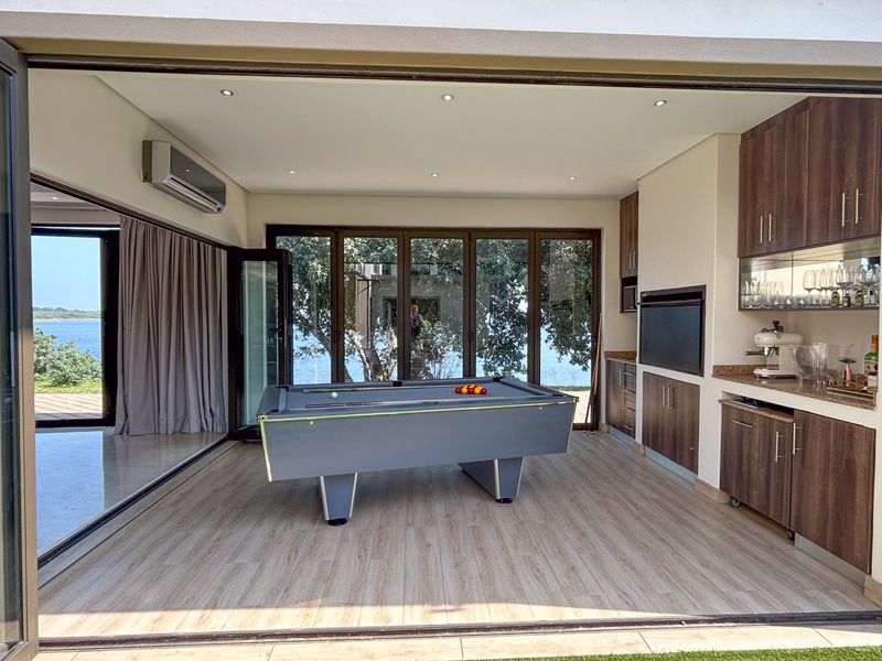 Modern entertainment room featuring built-in bar cabinetry, stone countertops, recessed lighting, and seamless indoor-outdoor flow through large stacking glass doors.