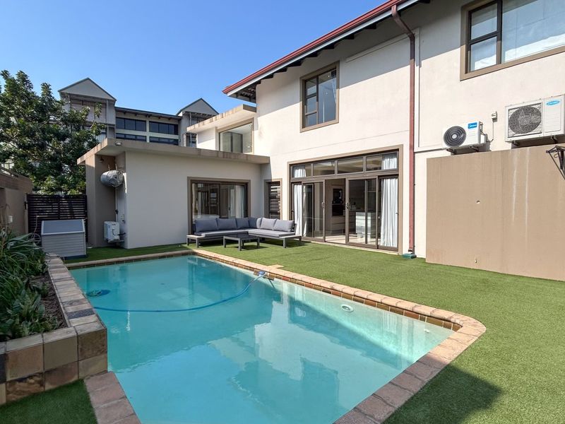 Rear exterior view featuring a swimming pool, artificial lawn, and direct access to the home via sliding glass doors.