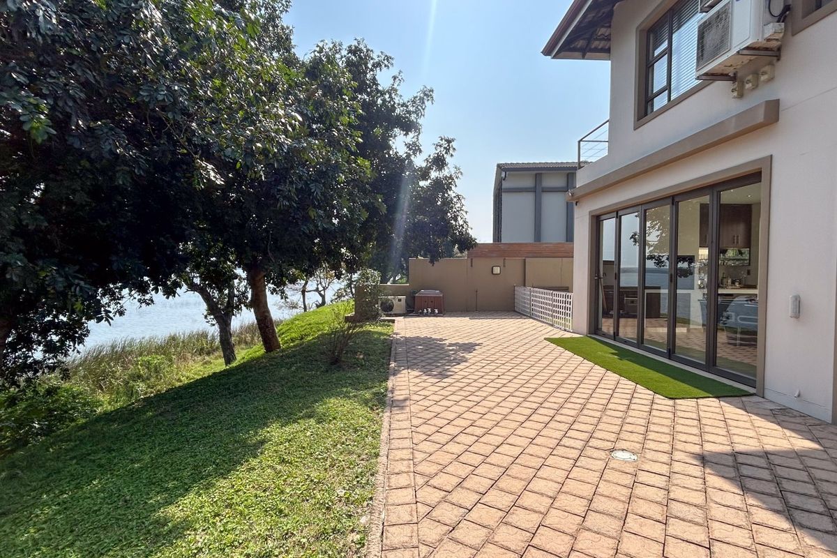 Spacious rear paved patio area featuring large sliding glass doors, overlooking a landscaped garden and waterfront view.