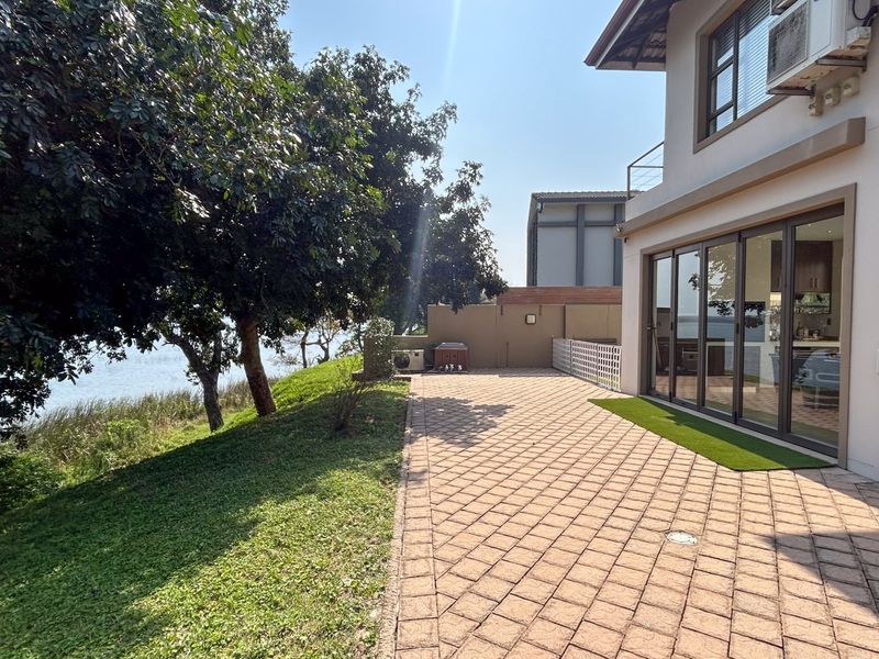 Spacious rear paved patio area featuring large sliding glass doors, overlooking a landscaped garden and waterfront view.