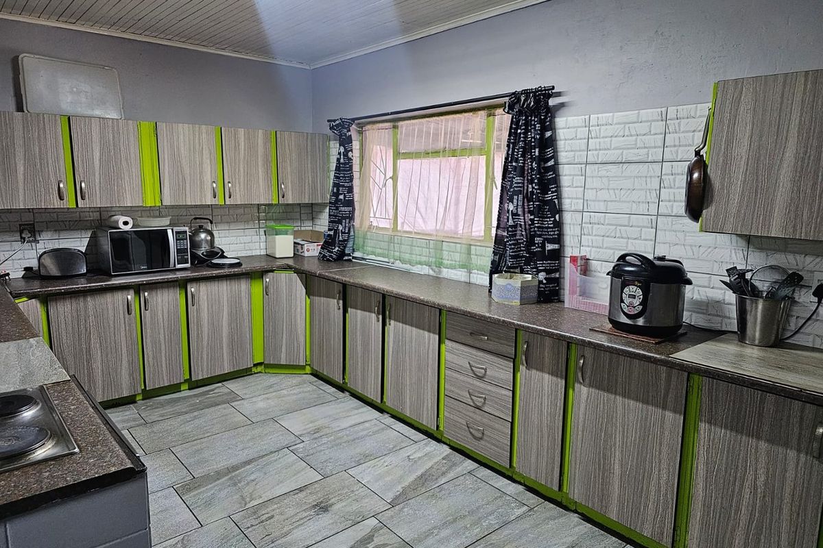 A functional kitchen featuring wood-grain cabinetry with lime green accents, tiled flooring, and a built-in cooktop.