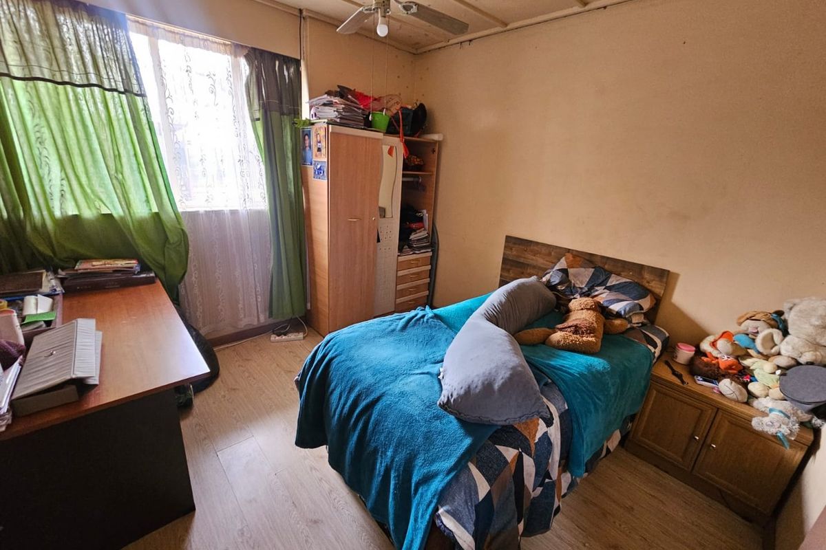 A bedroom featuring wood-look flooring, a ceiling fan, and a window with natural light, offering a functional space for rest.