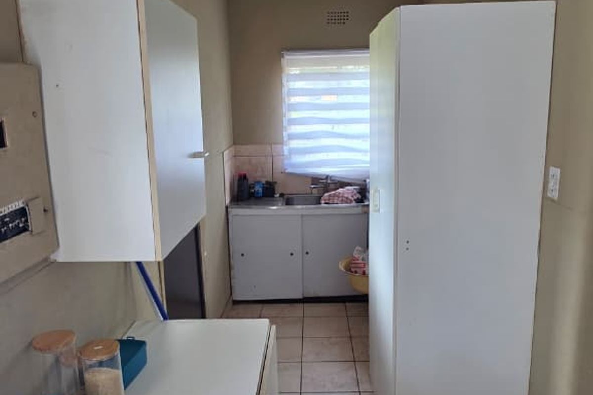A narrow galley-style kitchen featuring basic cabinetry, tiled flooring, and a single sink unit with a window providing natural light.