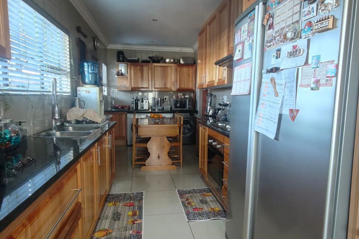 A functional galley-style kitchen featuring timber cabinetry, dark granite countertops, tiled flooring, and integrated oven and hob.