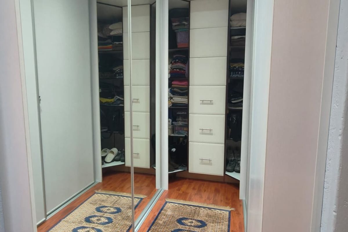 A well-organized walk-in closet featuring floor-to-ceiling built-in cabinetry with mirrored sliding doors and integrated shelving units.