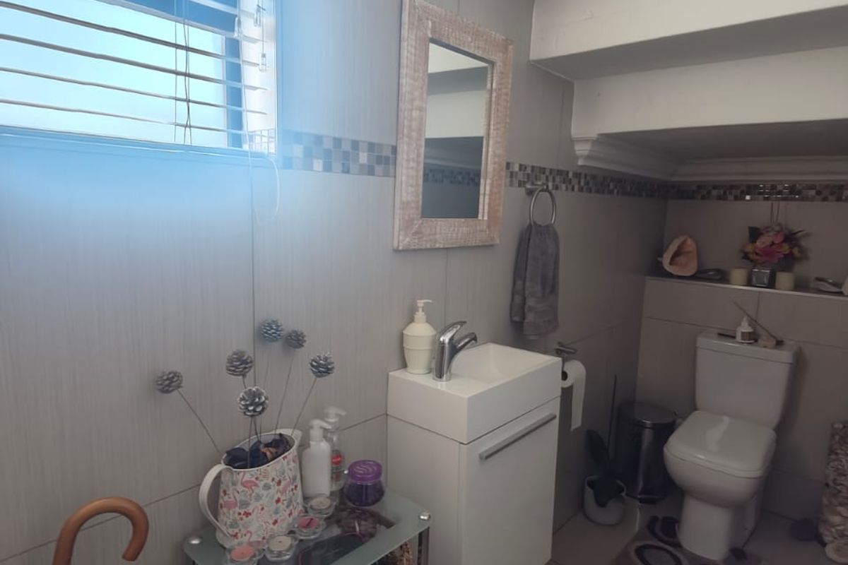 A compact bathroom featuring a wall-mounted vanity with basin, a modern toilet, and tiled walls with a decorative mosaic border.