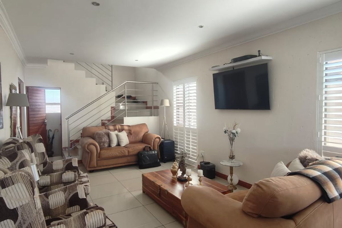 Spacious living room featuring tiled flooring, white plantation shutters, and a modern staircase with stainless steel balustrades.