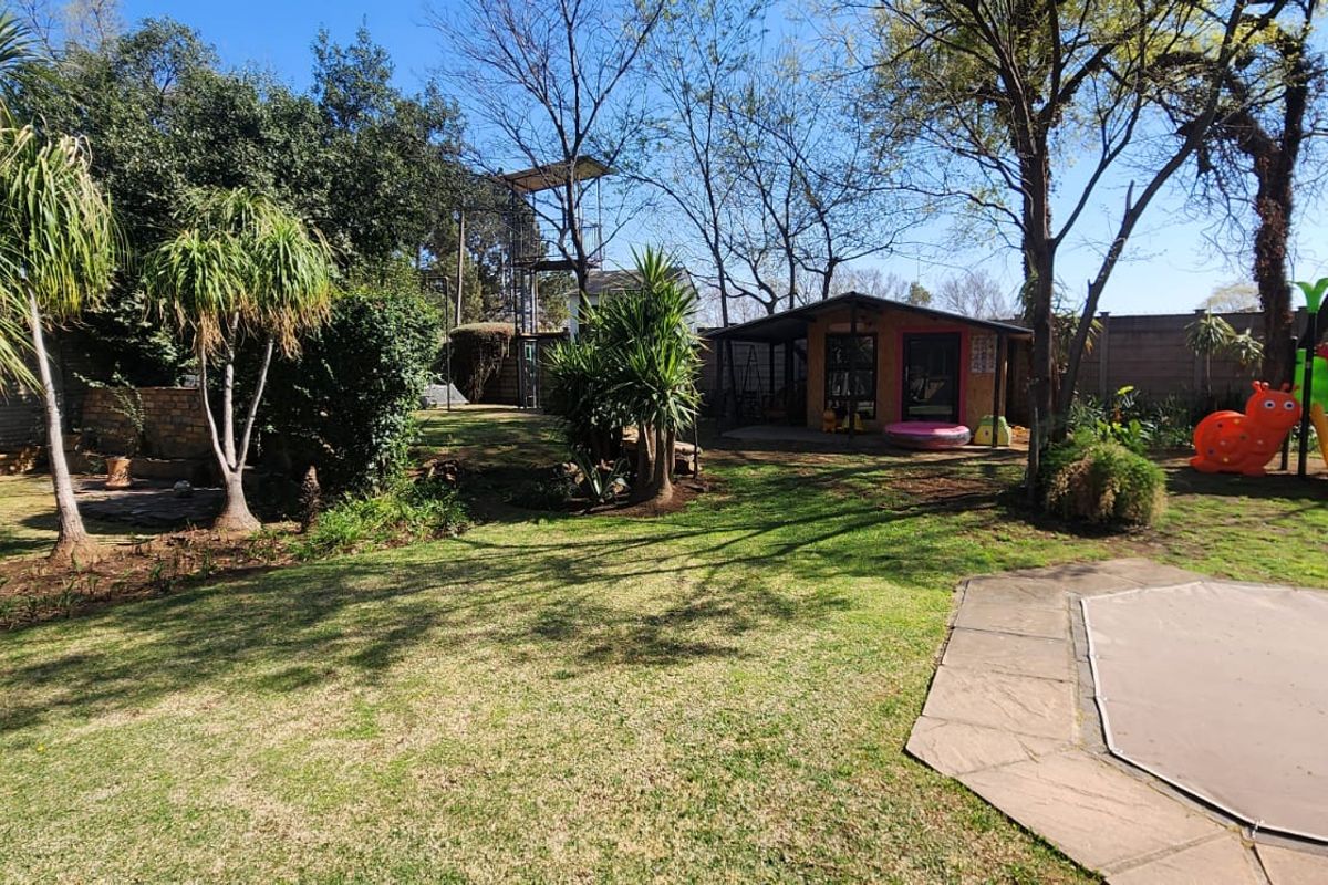 Spacious rear garden featuring a lawn, mature trees, a covered pool area, and a detached outbuilding structure.
