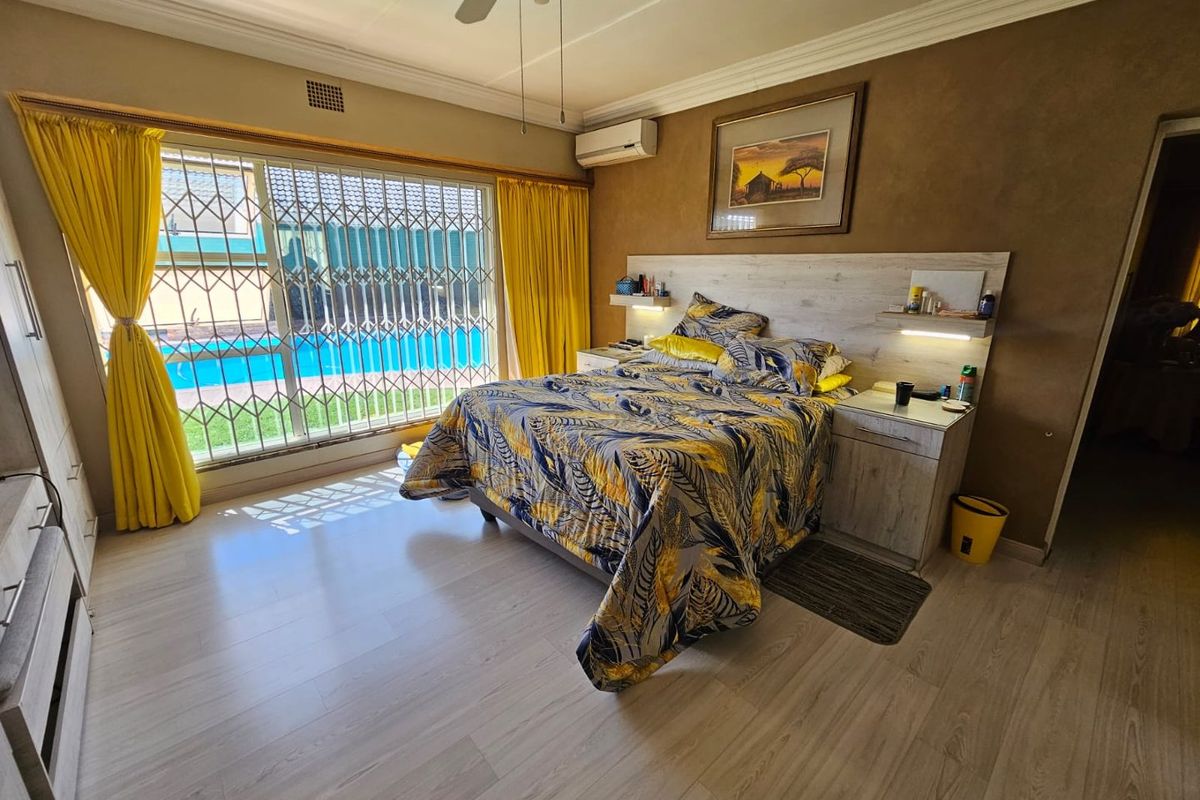 Spacious bedroom featuring light wood-look flooring, built-in headboard with integrated lighting, ceiling fan, and large sliding doors with security gates overlooking the pool area.