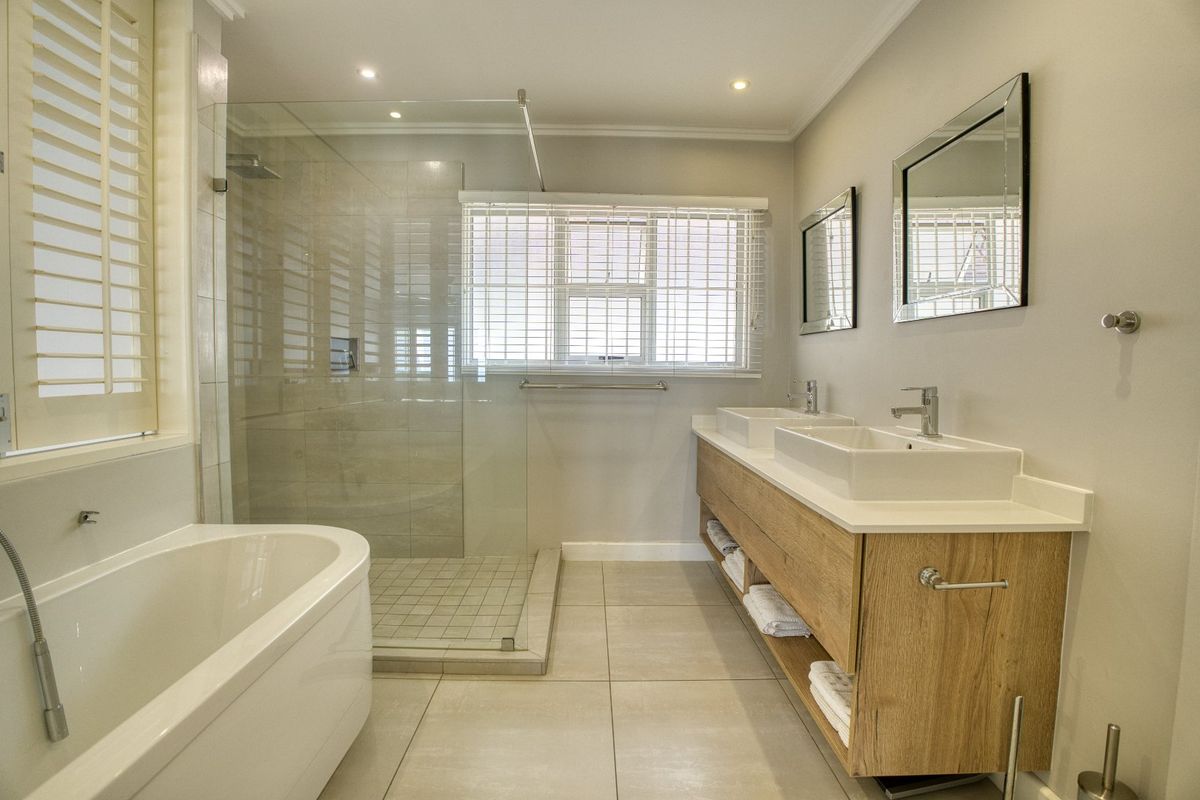 Modern bathroom featuring a double vanity with vessel sinks, a spacious glass-enclosed shower, and a sleek freestanding bathtub with neutral tile finishes.