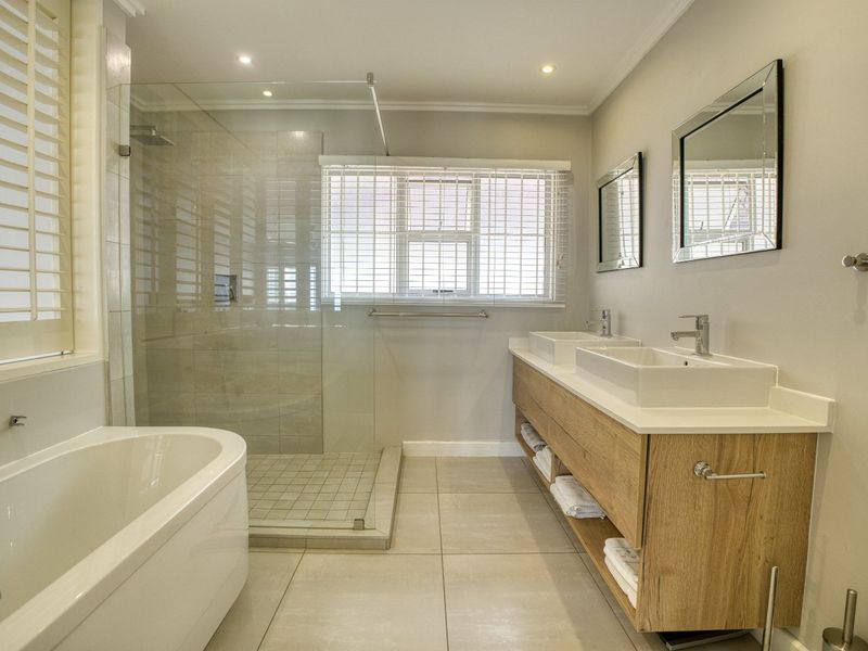 Modern bathroom featuring a double vanity with vessel sinks, a spacious glass-enclosed shower, and a sleek freestanding bathtub with neutral tile finishes.
