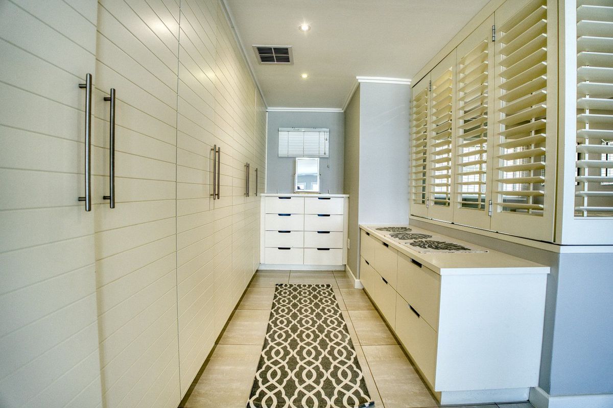 A well-appointed dressing room or walk-in closet featuring extensive built-in cabinetry, plantation shutters, and modern tiled flooring.